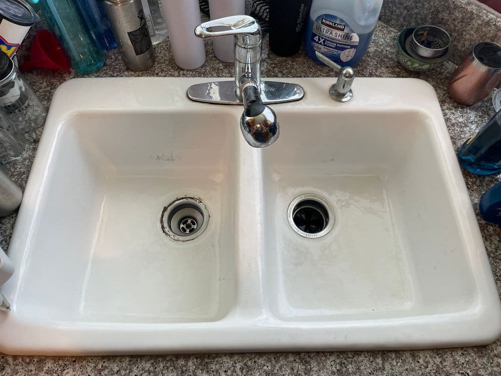 Double kitchen sink with a chrome faucet, surrounded by various kitchen items.