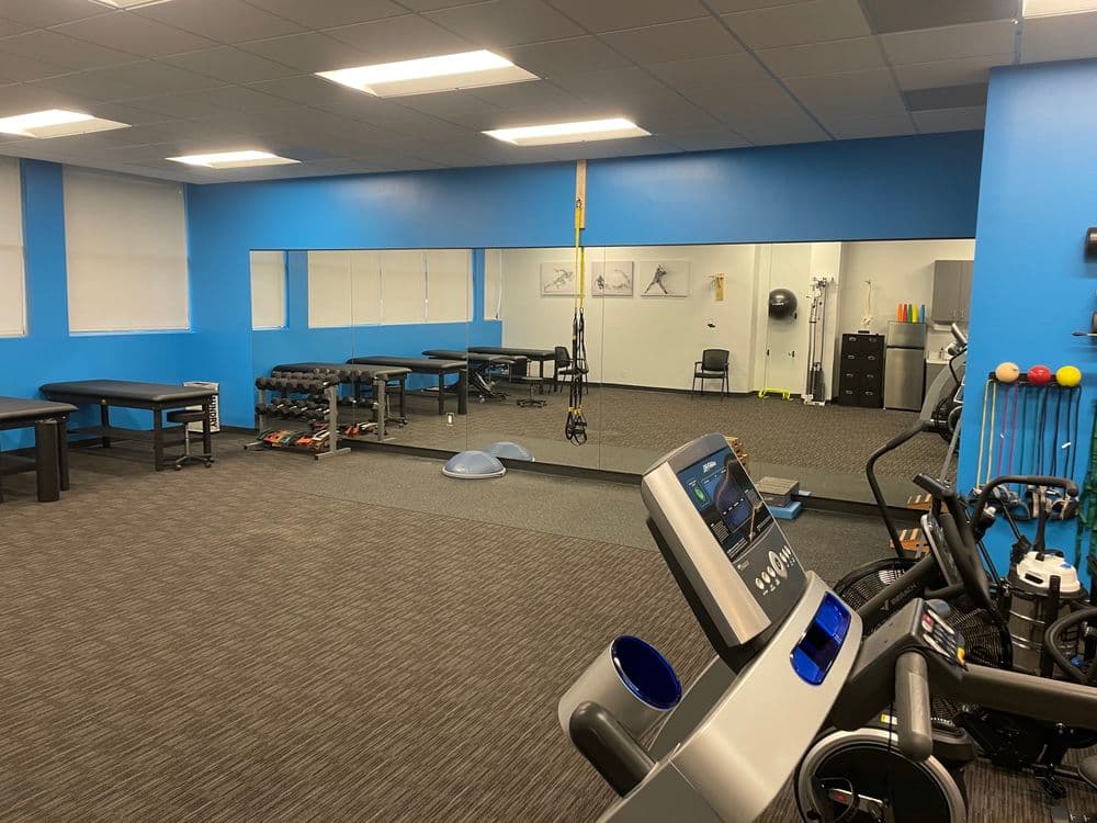 Modern fitness studio with cardio equipment, weight benches, and mirrored wall.