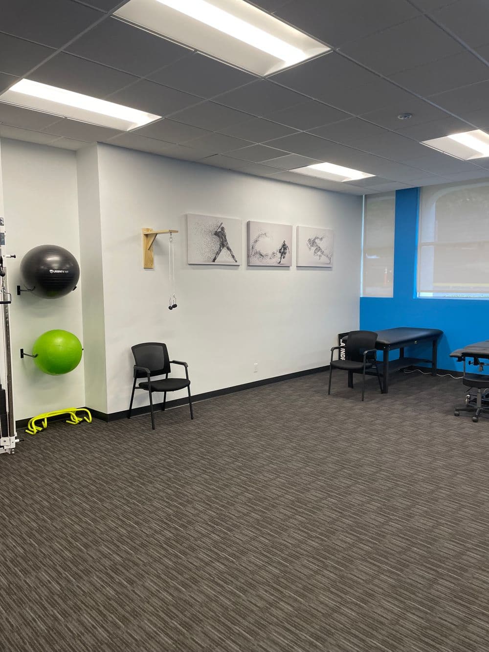 Empty therapy room with exercise equipment, wall art, and chairs for clients.