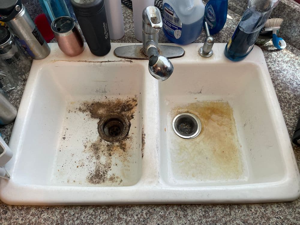 Dirty kitchen sink with grime in one basin and slightly cleaner water in the other basin.